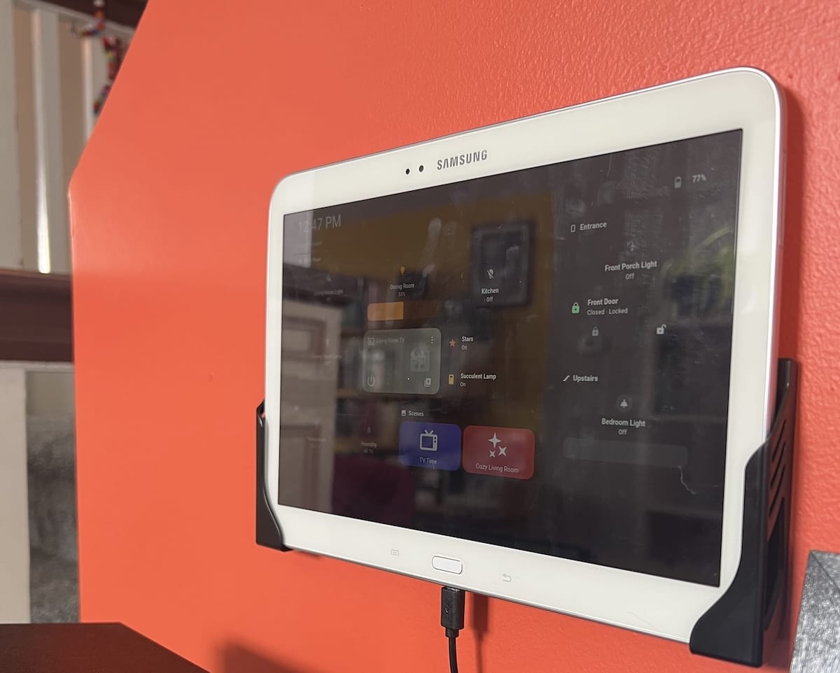 tablet device mounted on a wall; there is a glare on the screen but you can see some of a home assistant dashboard on it.