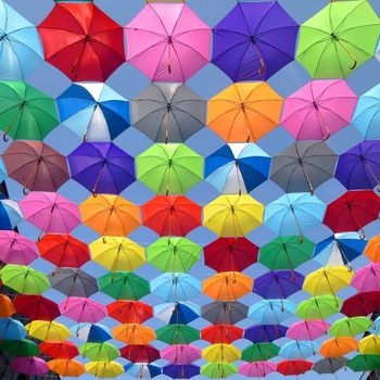 rainbow colored umbrellas between two roofs, against a blue sky